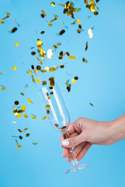 Free photo hand holding a glass surrounded by golden sequins and confetti