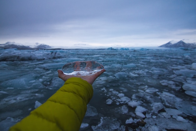 Free photo hand holding ice with a frozen sea under a cloudy sky in iceland on the background