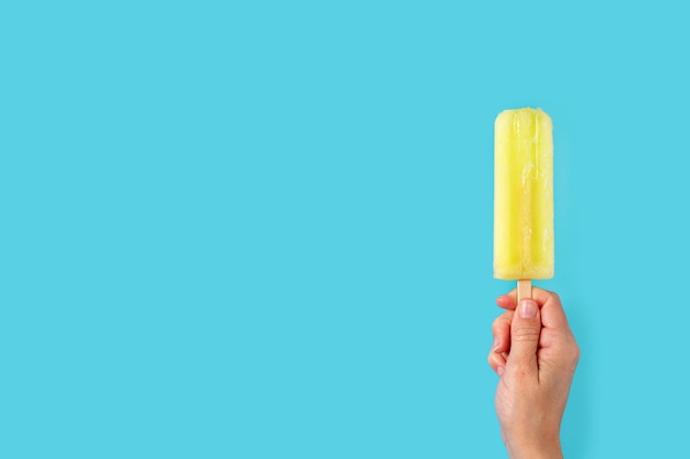 Free photo hand holding a lemon popsicle on blue background