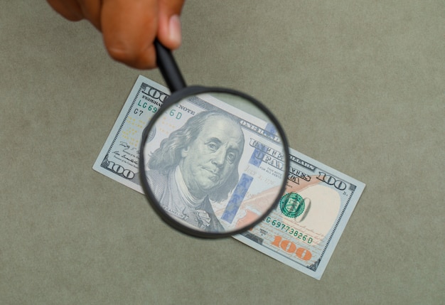 Free photo hand holding magnifying glass over banknote.