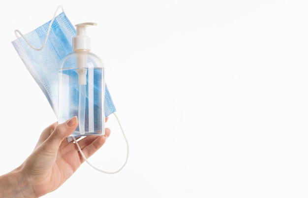 Hand holding medical mask with hand sanitizer bottle