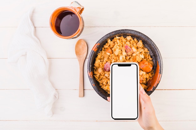 Free photo hand holding mobile on table with dish