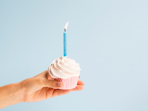 Hand holding muffin with blue candle