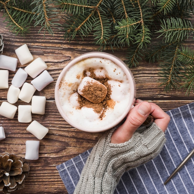 Hand holding mug with drink and marshmallows