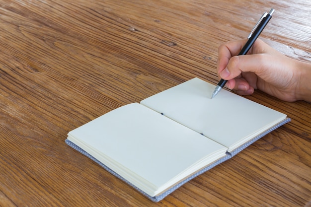 Hand holding a pen next to a blank notebook