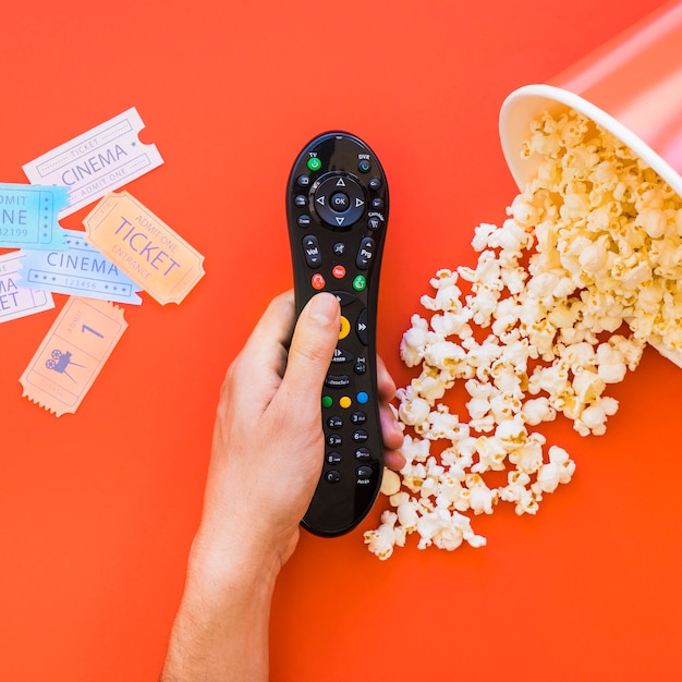 Free Photo hand holding remote control over popcorn and movie tickets