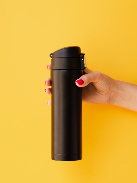 Free Photo hand holding thermos mock-up on yellow background