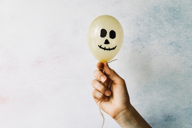 Free Photo hand holding white balloon with scary face