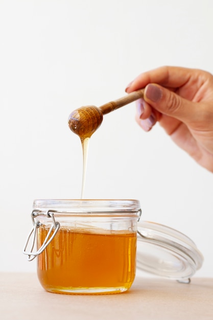 Free Photo hand holding wooden honey dipper from honey jar