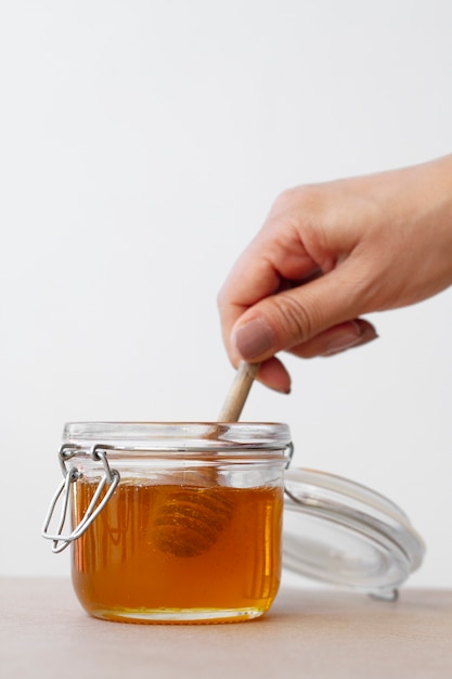 Hand holding wooden honey dipper from honey jar