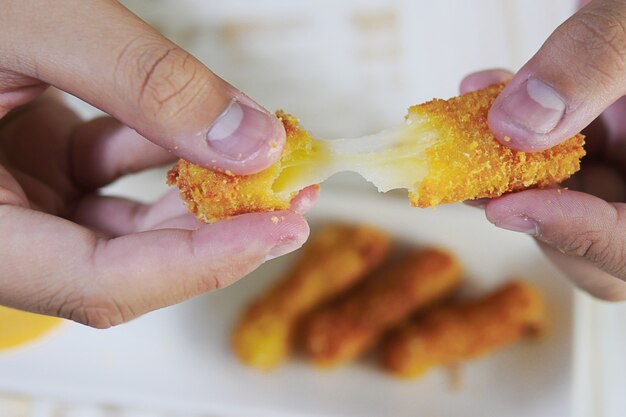 Hand is holding a stretch cheese ball ready to be eaten with soft focused french fries 