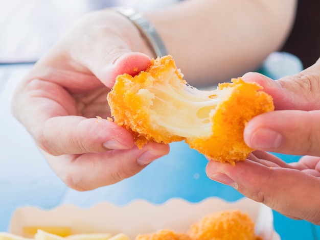 Hand is holding a stretch cheese ball ready to be eaten with soft focused french fries 