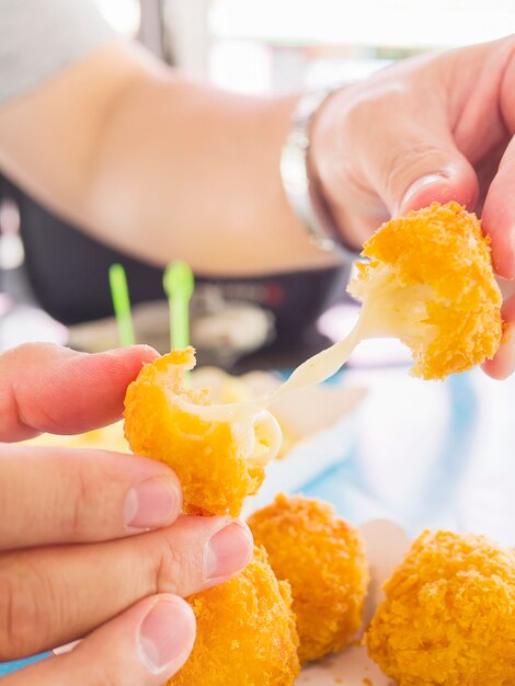 Hand is holding a stretch cheese ball ready to be eaten with soft focused french fries