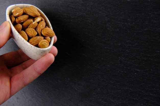 Hand is holding a white plate full of brown almonds on black