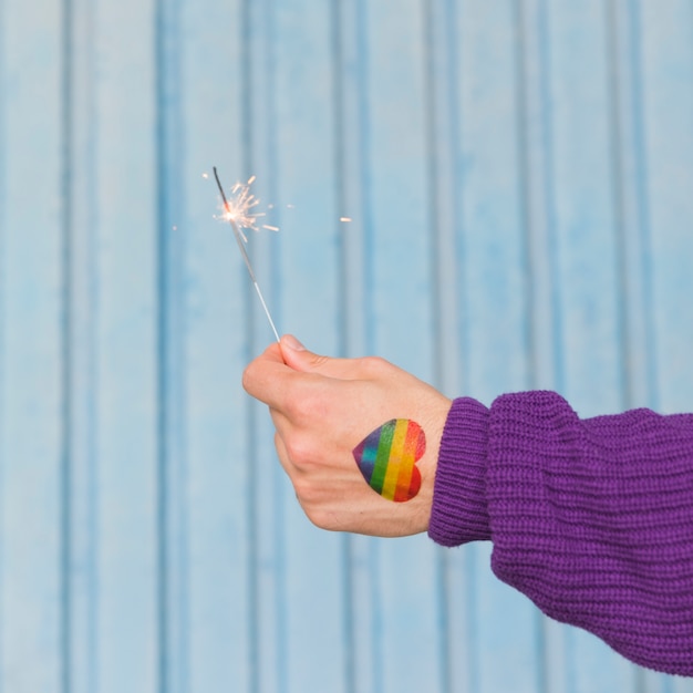 Free photo hand of man with rainbow heart holding sparkler