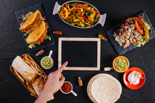 Hand pointing at blackboard amidst Mexican food