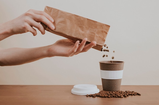 Free photo hand pouring coffee beans from a paper bag into a coffee cup