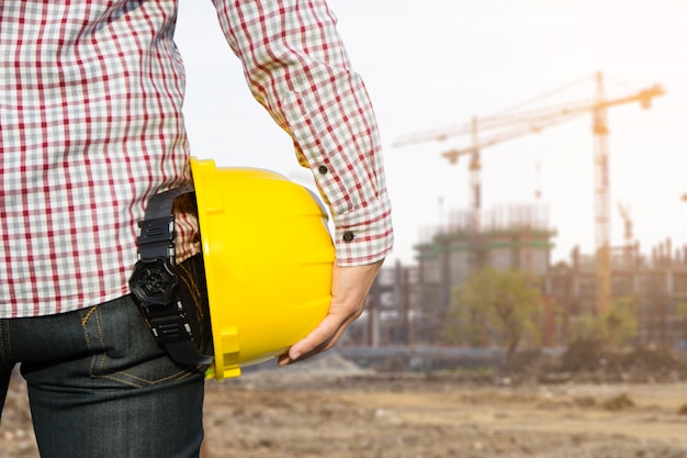 Free photo hand's engineer worker holding yellow safety helmet with building on site background.