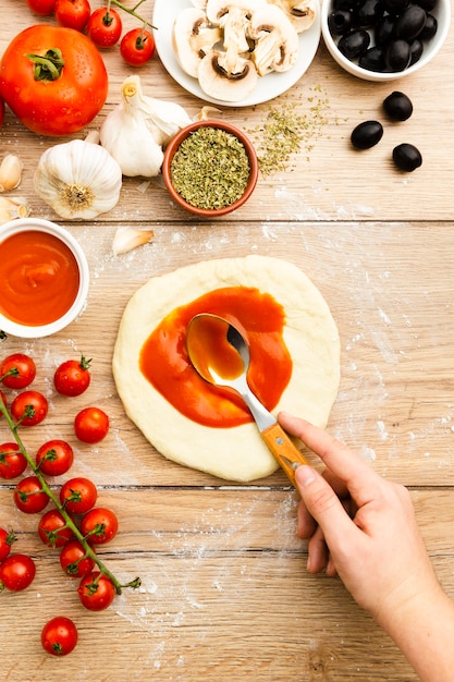 Free photo hand spreading tomato sauce on pizza dough