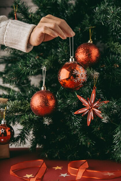 Hand of unrecognizable woman holding bauble in front of Christmas tree