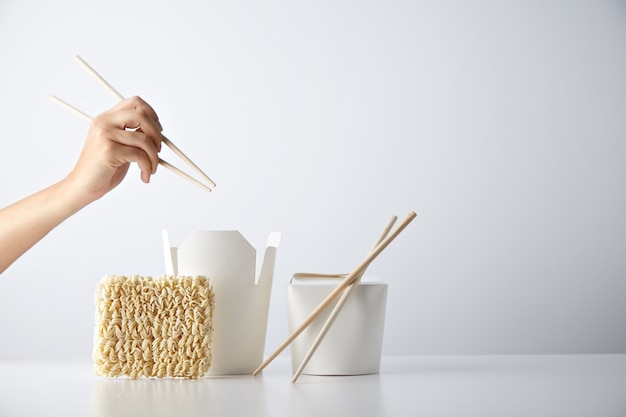 Hand with chopsticks ready above opened and closed takeaway boxes