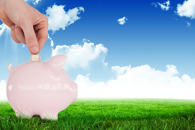 Hand with a coin over a pink piggy bank