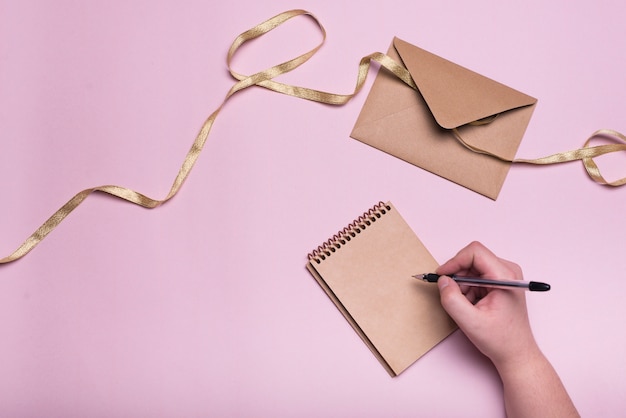 Hand with pen near notebook, envelope and ribbon