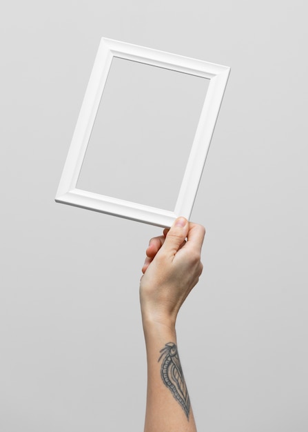 Hand with tattoo holding empty white frame