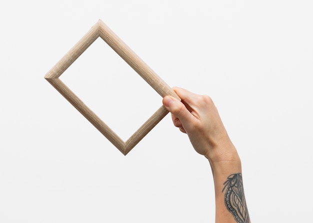 Free photo hand with tattoo holding wooden frame