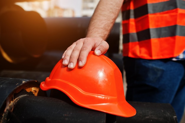 Hand of worker man in safety orange helmet near steel pipes