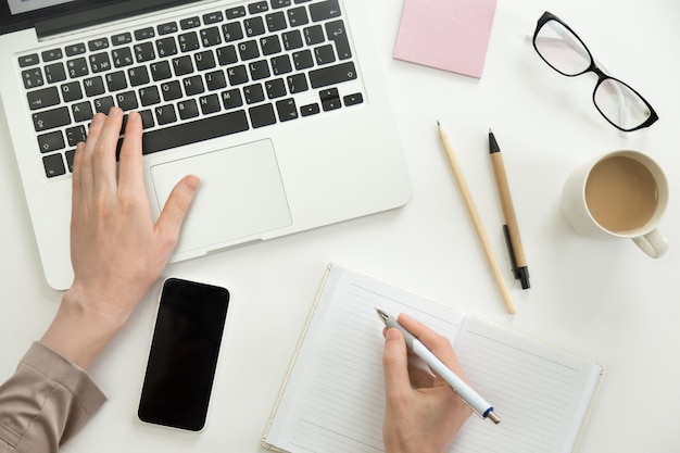 Hand working on a laptop, another holding a pen