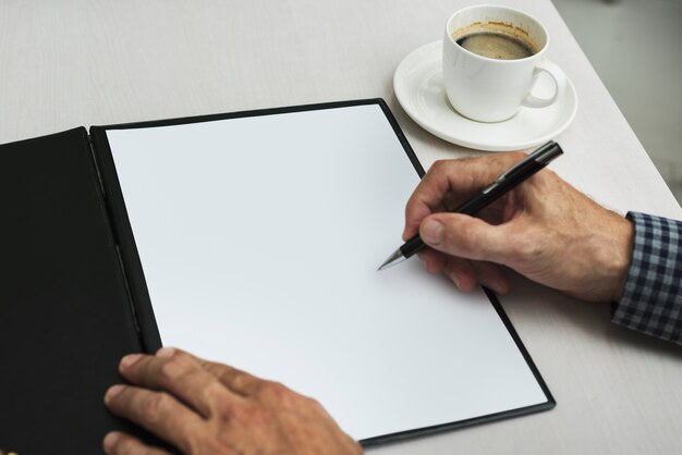 Hand writing in blank paper next to coffee cup