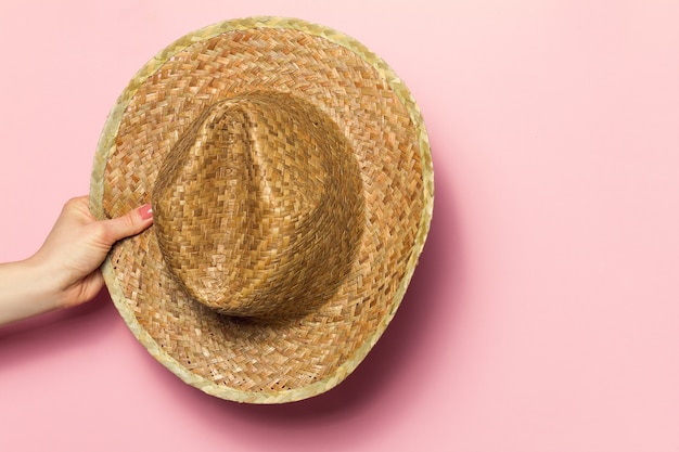 Free photo hand of young woman holding summer straw hat on pink background. fashion background. summer concept.