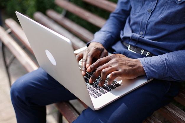 Hands of African American man typing something on the laptop while he sits on the bench