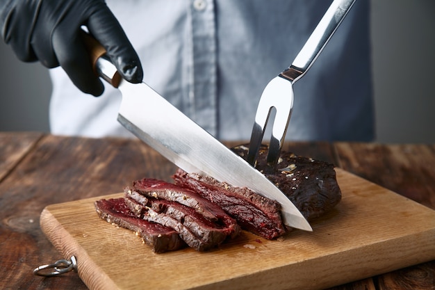 Free Photo hands in black gloves slice medium rare cooked whale meat steak with knife and fork