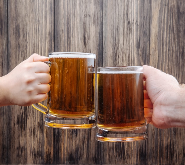 Free photo hands clinking mugs of beer on rustic wood side view