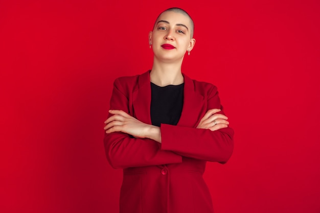 Free photo hands crossed. portrait of young caucasian bald woman isolated on red wall. beautiful female model in jacket. human emotions, facial expression, sales, ad concept. freaky culture.