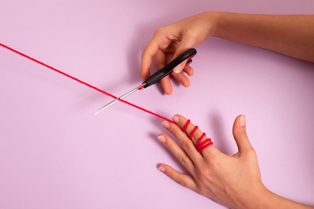 Hands cutting red thread with scissors