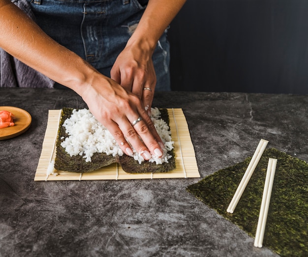 Hands dividing rice evenly on nori