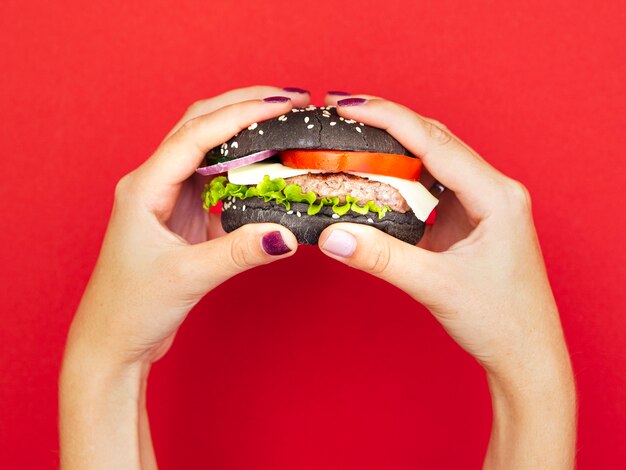 Free Photo hands holding appetizing burger with red background