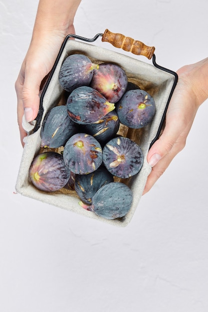 Free photo hands holding a basket of purple figs on white