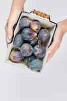 Free photo hands holding a basket of purple figs on white