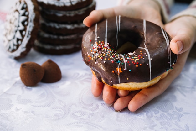 Free photo hands holding chocolate donut with sprinkle on table cloth