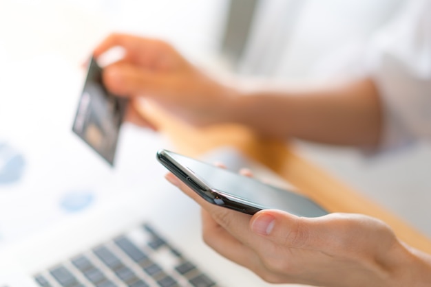 Hands holding a credit card using laptop computer and mobile phone for online shopping