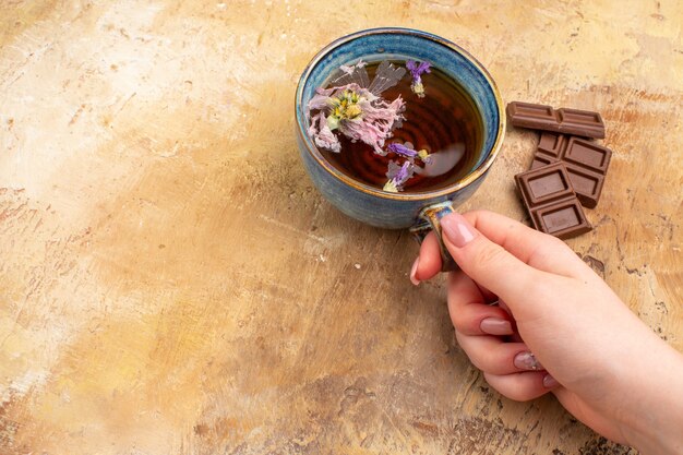 Hands holding a cup of hot herbal tea and chocolate bars on mixed color table