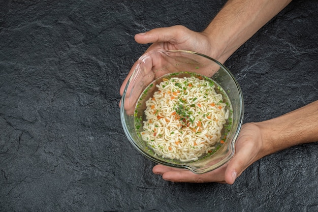 Free Photo hands holding a glass plate with delicious noodles on a dark surface.