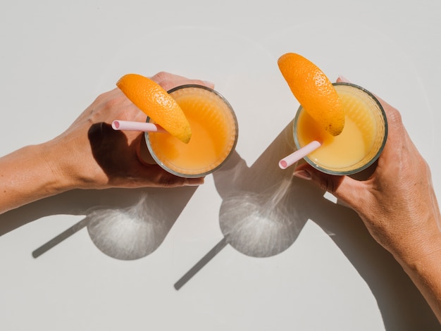 Hands holding glasses with natural orange juice top view