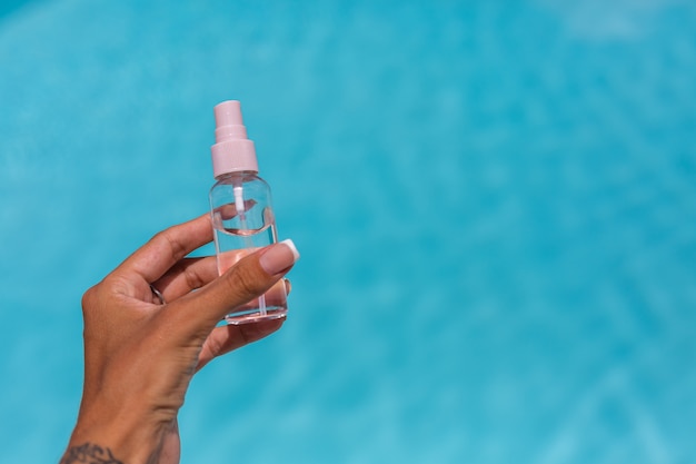 hands holding small bottle of tanning oil liquid over blue swimming pool