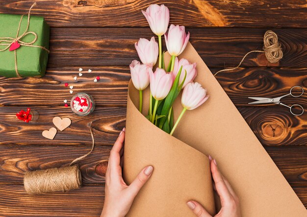 Hands packaging flowers on wooden table 