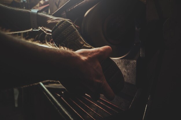 Hands of shoe master, which is working on shoe sole, using special machine tool.